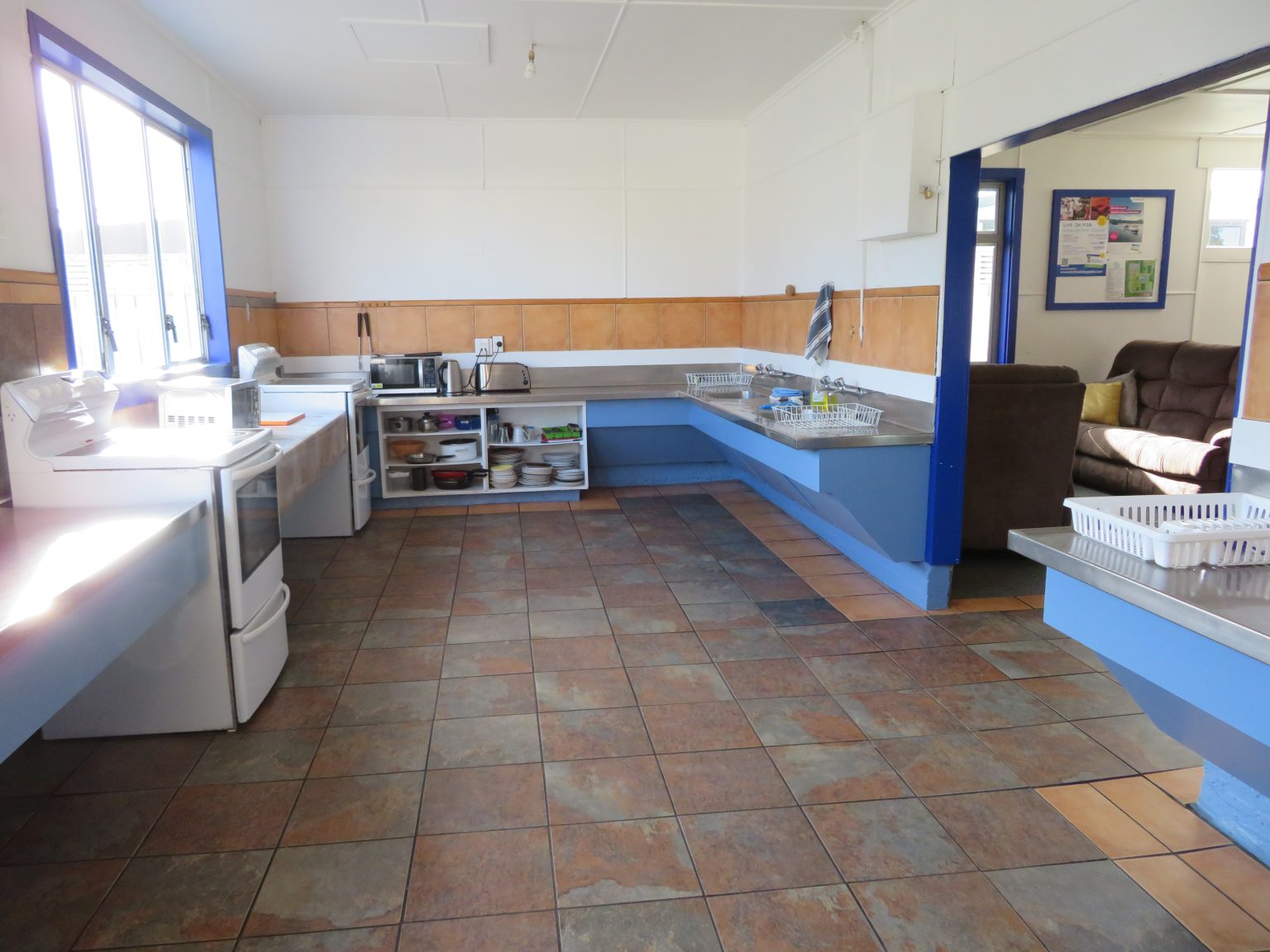Communal guest kitchen with ovens, benches, sinks and a dining area beyond