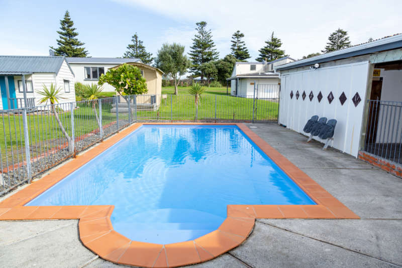 The outdoor swimming pool in the grounds of Whanganui Seaside Holiday Park, with cabins and trees behind